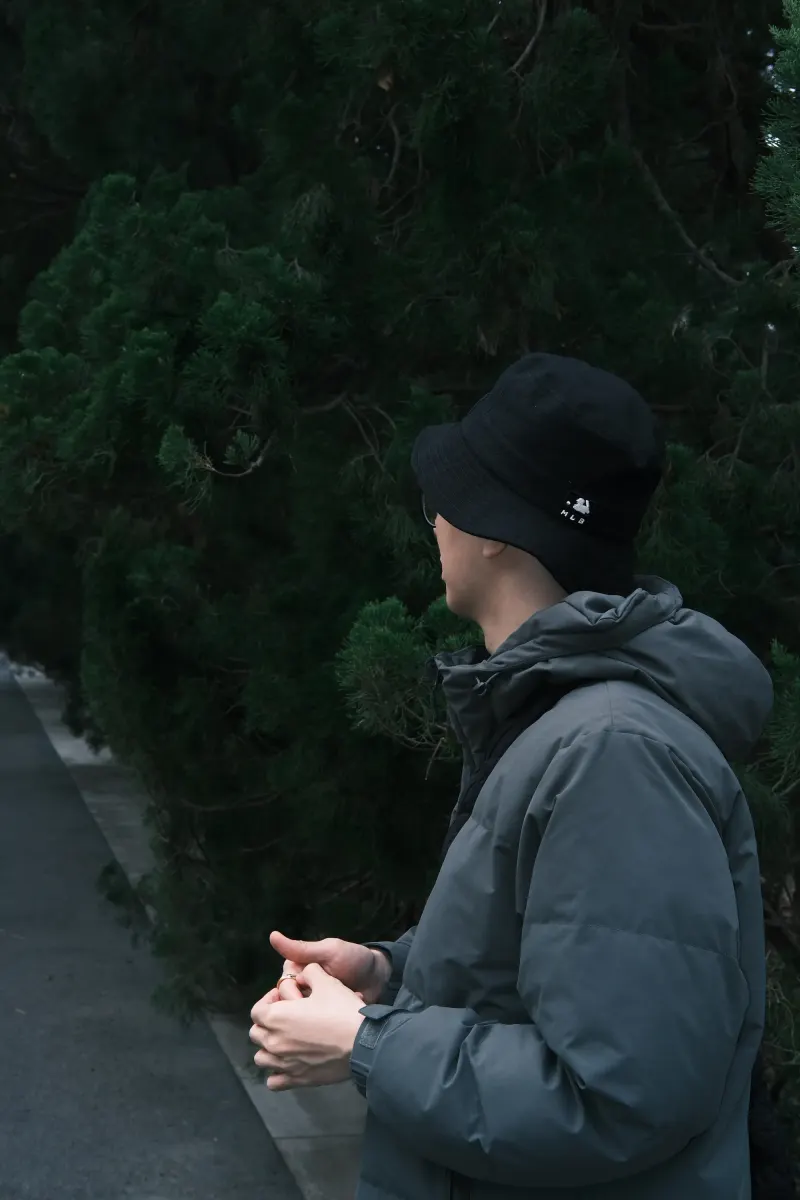 戴黑色渔夫帽的人站在常青树旁